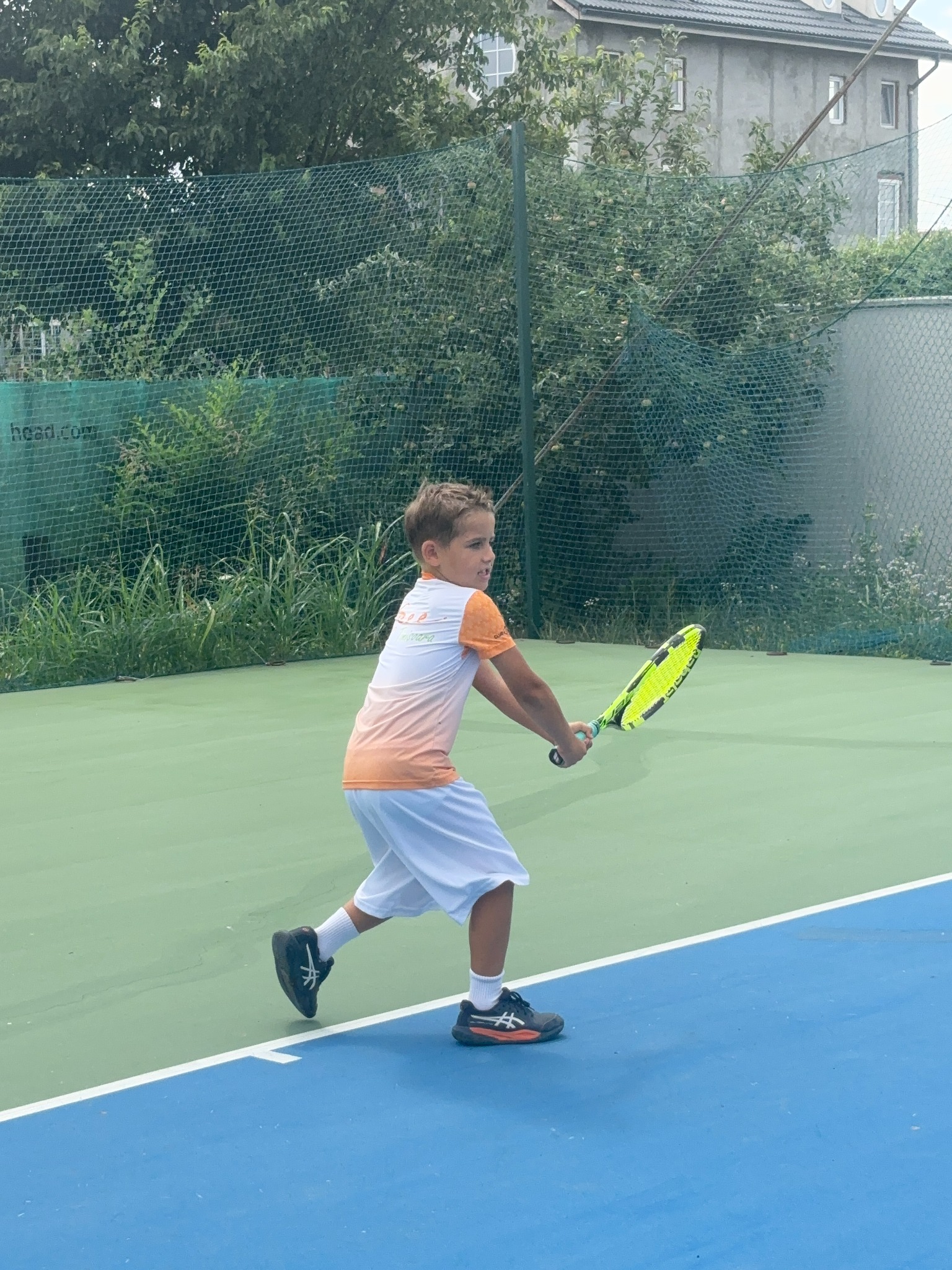 Copil exersând o lovitură pe terenul de tenis