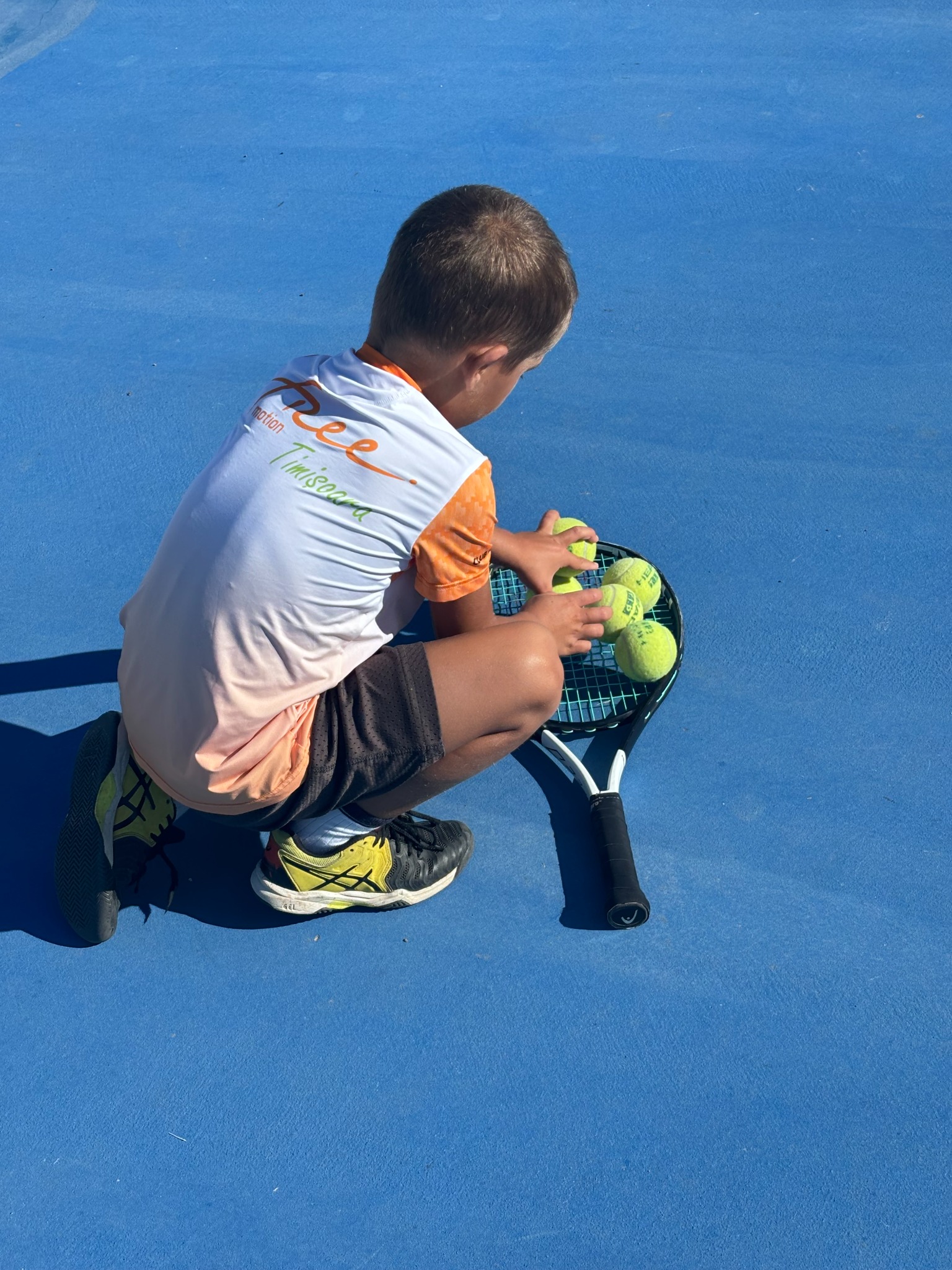 Copil cu racheta și mingi de tenis pe terenul albastru